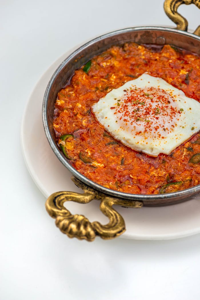 Tasty shakshuka dish with poached egg in a copper pan, garnished beautifully, served on a white plate.